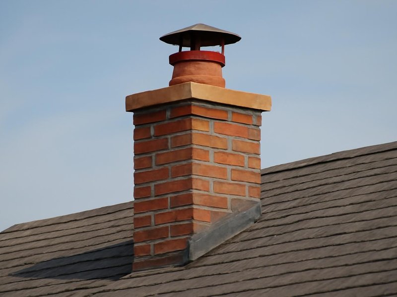 AI concept: A real-looking brick chimney on a shingle roof with visible open clay flue extending above the crown and a raised metal rain cap with clear ventilation gap